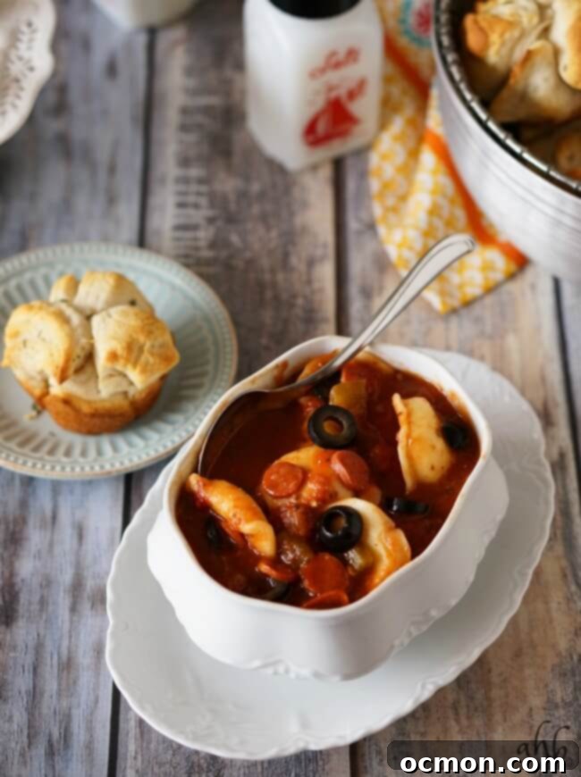 Scooping a spoonful of pepperoni pizza soup from a pot, highlighting the mini pepperonis and rich broth