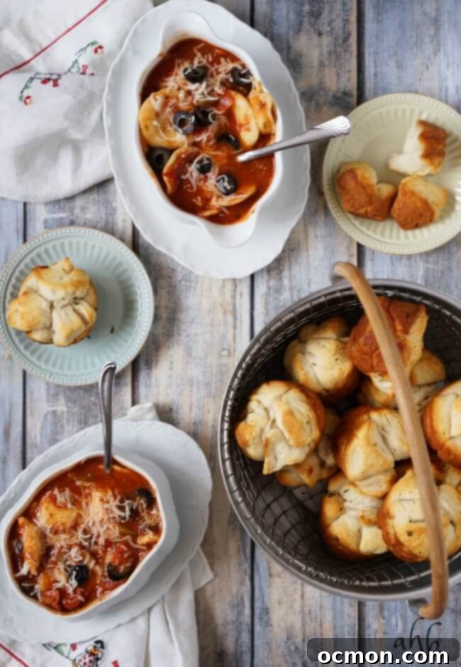 Overhead view of a bowl of pepperoni pizza soup with fresh mozzarella, black olives, and herbs, served with garlic bread pull-aparts
