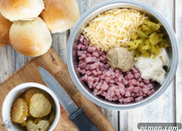 Ham, deli mustard, swiss cheese, mayo, and pickles in a mixing bowl ready to be stirred.