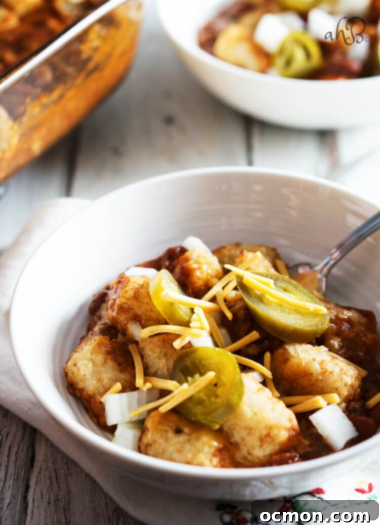 Loaded Chili Cheese Tater Tot Bake 8 A white bowl with a serving of Chili Cheese Tater Tot Casserole, topped with chopped onions and jalapenos.