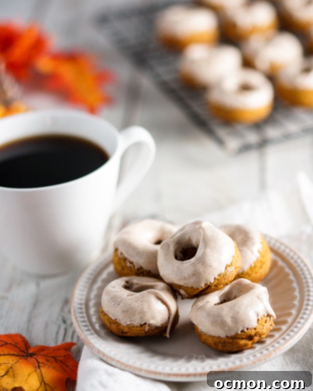 Spiced Pumpkin Cream Cheese Donuts 2 Close-up of baked mini pumpkin roll donuts with cinnamon cream cheese glaze, stacked on a white plate
