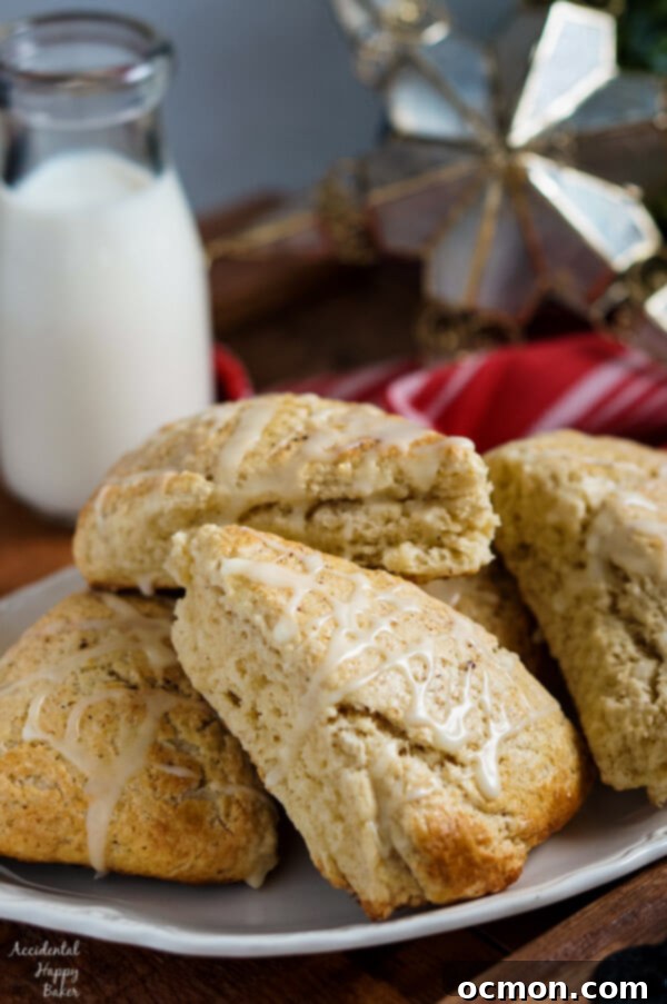A festive holiday setting with two Eggnog Scones on a plate, one partially eaten, showing its soft interior, next to a cup of coffee