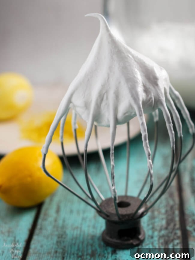 A whisk lifting a fluffy, white lemon meringue cookie batter from a mixing bowl, showing its light texture.