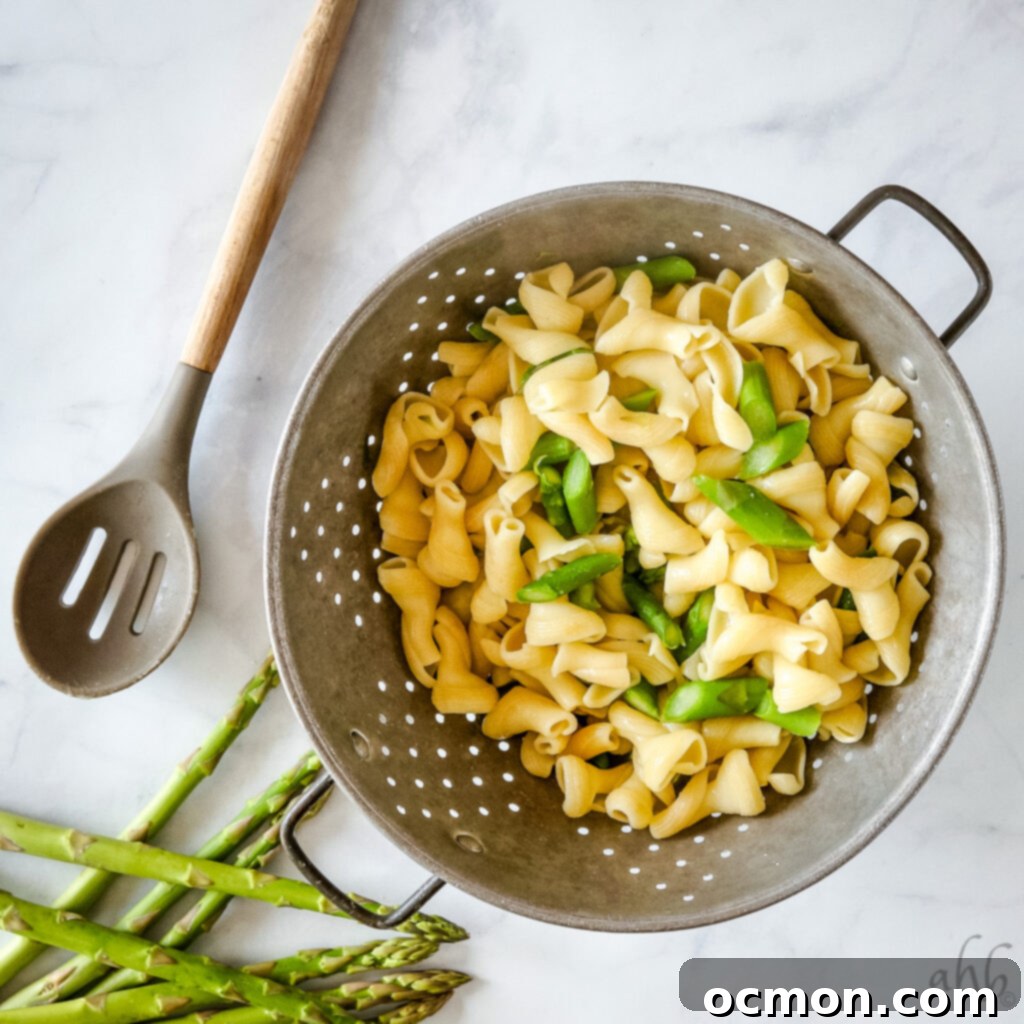 Close-up of creamy pesto pasta salad showing pasta, asparagus, and cherry tomatoes coated in dressing.