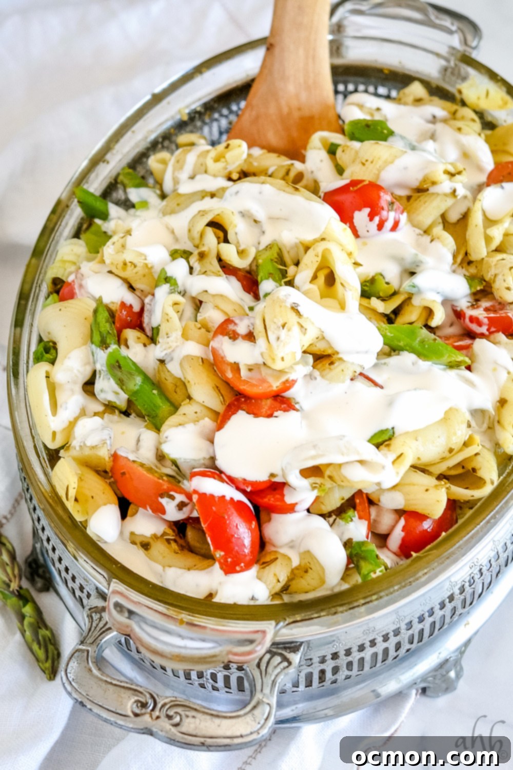 A serving dish of creamy pesto pasta salad drizzled with homemade creamy dressing.