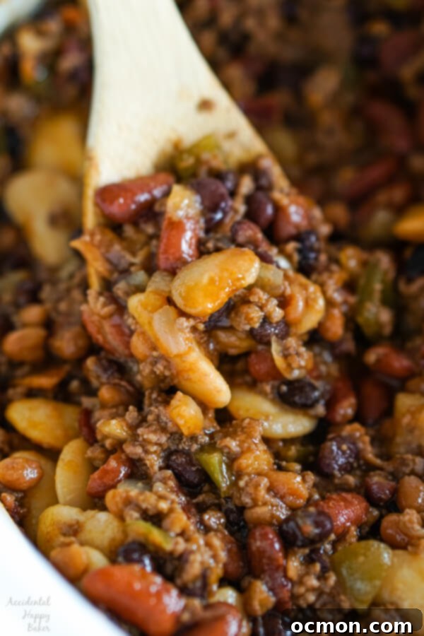 A close-up shot of Slow Cooker Calico Beans with a spoon, highlighting the rich sauce, tender beans, and bits of ground beef and bacon.