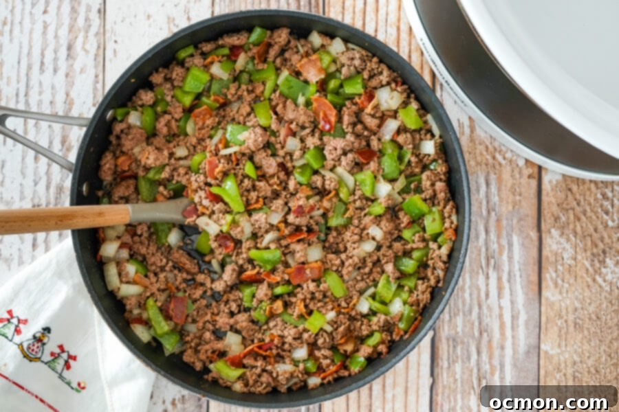 Ground beef, diced onion, and green pepper browning in a skillet for slow cooker calico beans, surrounded by the crispy bacon bits.