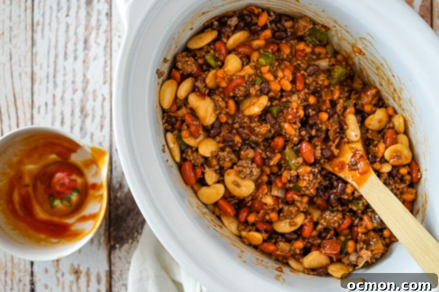 The slow cooker filled with calico beans, ground beef, and bacon, with the sauce mixed in, ready for cooking and simmering.