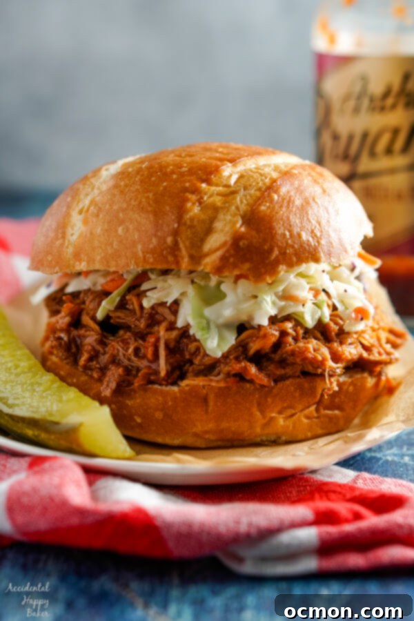 A pulled pork sandwich topped with coleslaw sitting beside a dill pickle.