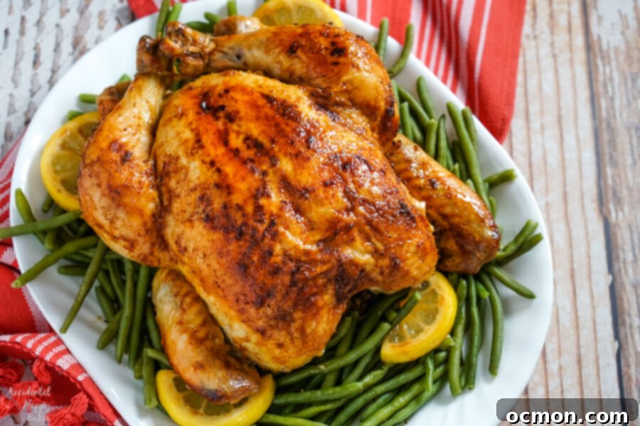 A roasted chicken rests on a bed of green beans with lemons on a white platter.