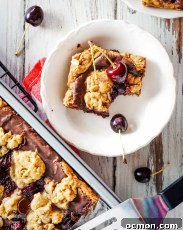 A cherry revel bar with a bite taken out of it sitting next to a pan of cherry revel bars. 