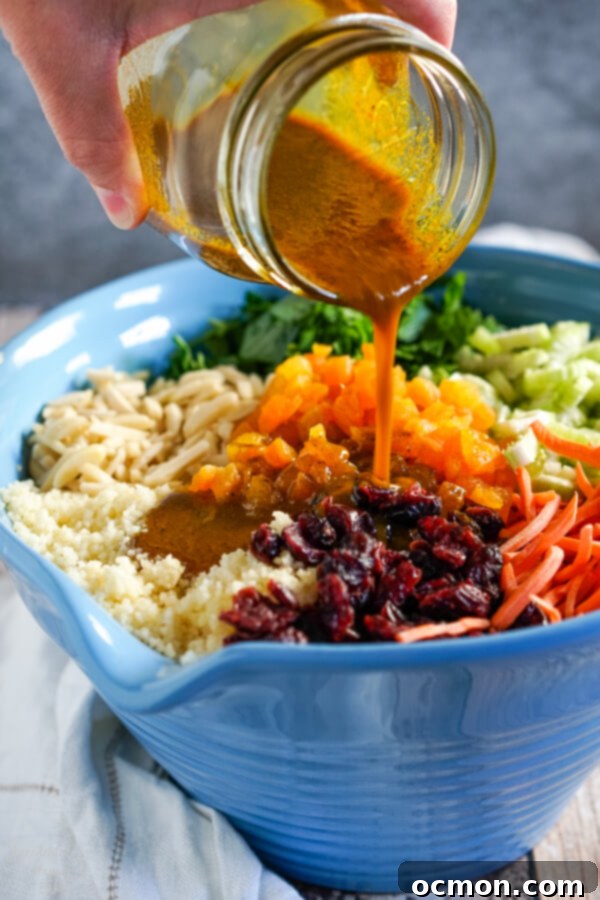 Golden Curried Couscous Salad 5 The vibrant yellow curry dressing being poured from a mason jar over a large bowl of curried couscous salad, ready to be mixed.