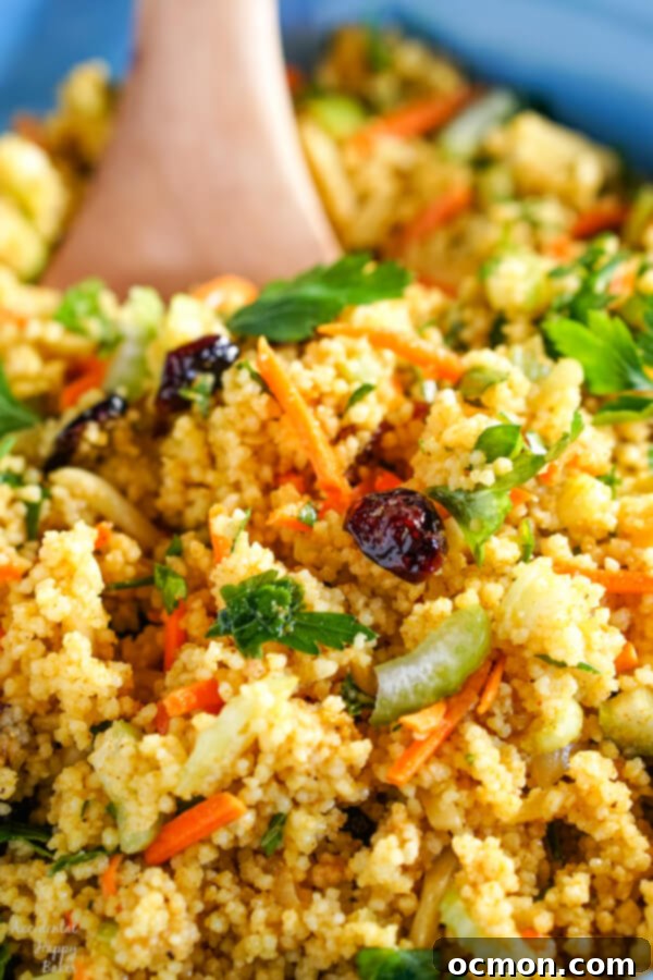 Golden Curried Couscous Salad 7 A closeup shot of curried couscous salad in a blue bowl with a wooden spoon.