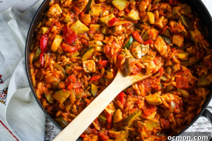 A large skillet filled with Italian Chicken and Orzo, all ingredients combined and gently simmering. This hearty and colorful one-pot dinner is almost ready.