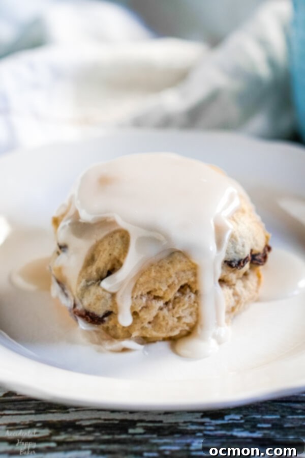 Delightful Cinnamon Raisin Biscuits 2 A cinnamon raisin biscuit, covered with creamy vanilla glaze on a white plate.