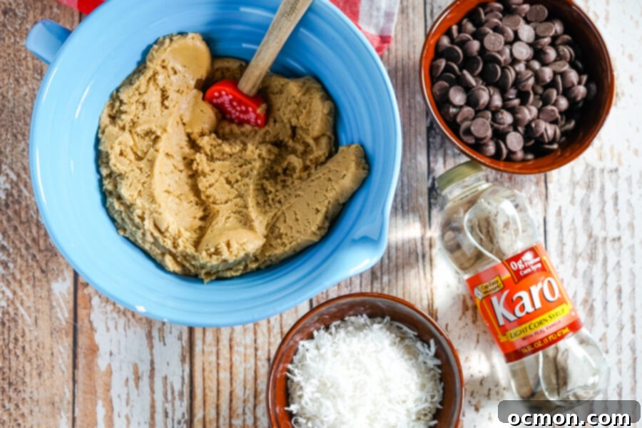 A blue bowl of cookie dough surrounded by a bowl of chocolate chips, coconut flakes, and Karo Corn Syrup