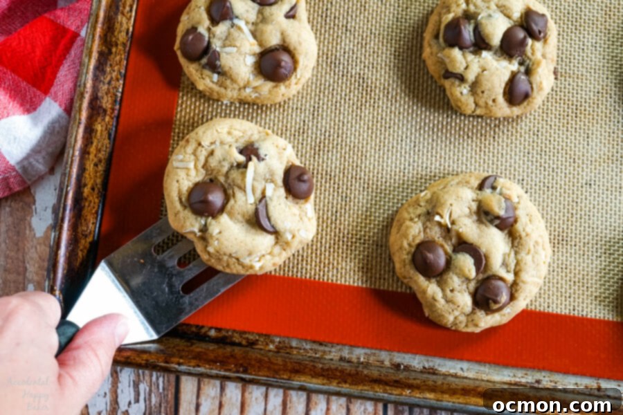 Removing a chewy coconut chocolate chip cookie off the baking tray.
