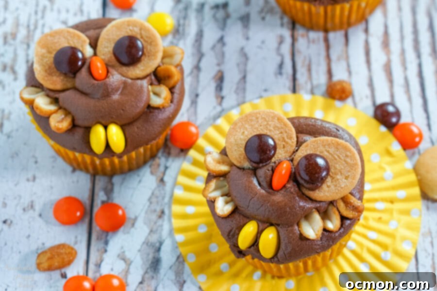 Hoot-Worthy Peanut Butter Chocolate Cupcakes 11 Two peanut butter chocolate owl cupcakes sit on a yellow cupcake wrappers surrounded by Reese's Pieces candy.