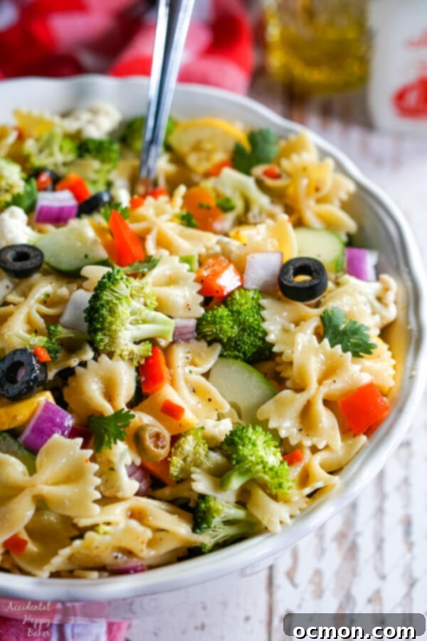 Vibrant Summer Veggie Pasta 3 A vertical shot of a white bowl overflowing with colorful Summer Vegetable Pasta Salad, ready to be served with a slotted spoon.