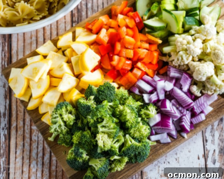 Vibrant Summer Veggie Pasta 5 A wooden cutting board loaded with neatly chopped yellow squash, red bell pepper, crisp cucumber, fresh broccoli florets, vibrant red onion, and white cauliflower, ready for the pasta salad.