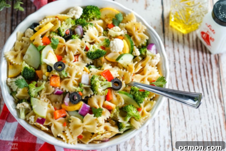Vibrant Summer Veggie Pasta 6 A close-up of a large white bowl filled with Summer Vegetable Pasta Salad, showcasing farfalle pasta, colorful veggies, and the glistening Italian dressing, with olive oil and a pepper grinder in the background.