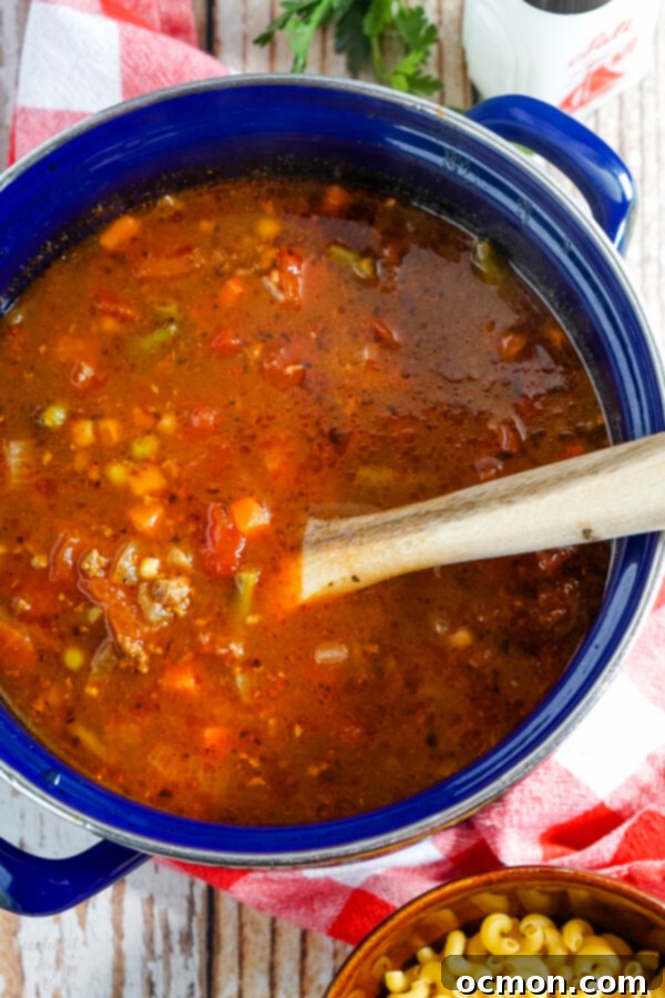 Mixed vegetables and diced tomatoes being added to the browned ground beef in a stockpot for hamburger macaroni soup.