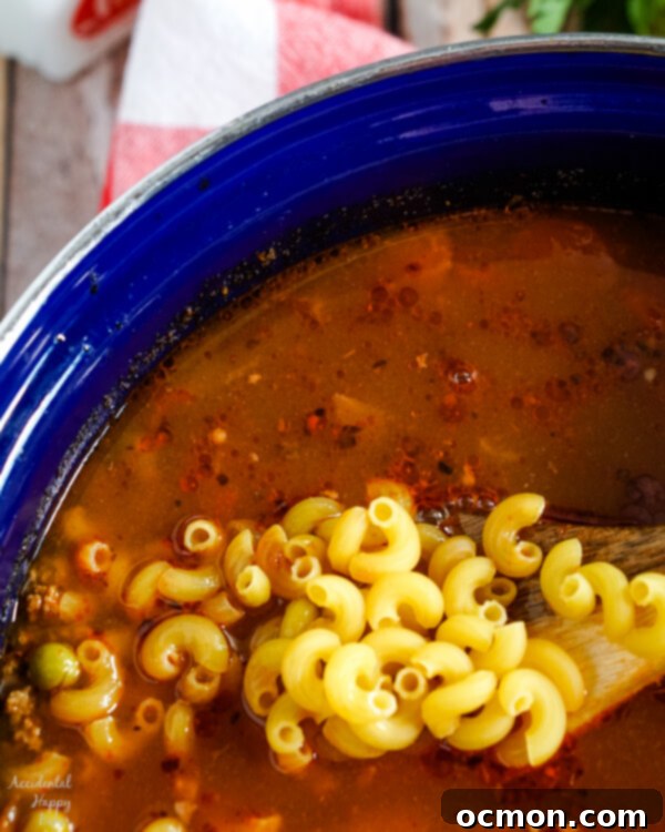 Adding elbow macaroni to a simmering pot of hamburger macaroni soup, showing the process of cooking the pasta in the broth.