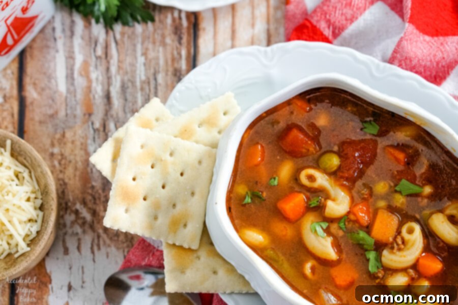A large bowl of hamburger macaroni soup ready to be served, alongside pull-apart garlic rolls, suggesting a complete, comforting meal.