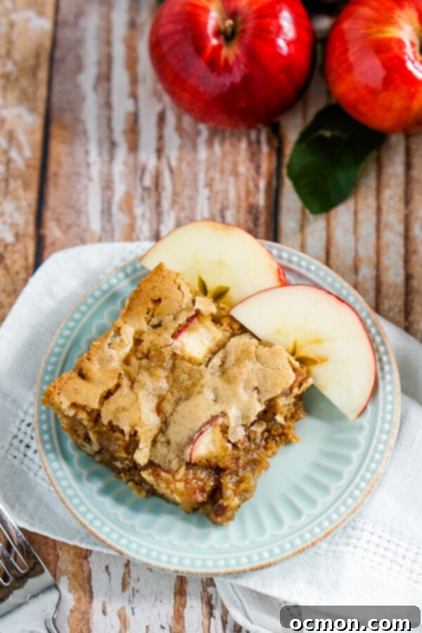 Two slices of golden-brown apple cinnamon bars on white plates, with a full pan of bars in the background. The bars are studded with apple pieces and pecans.