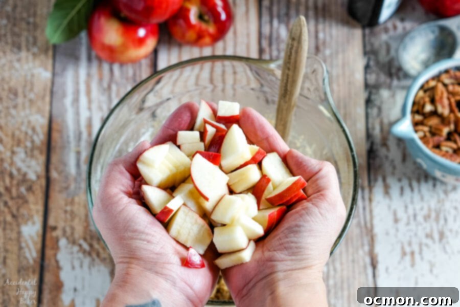 A close-up shot of freshly chopped apples, some with their vibrant red skin still on, in a mixing bowl, ready to be added to the batter.
