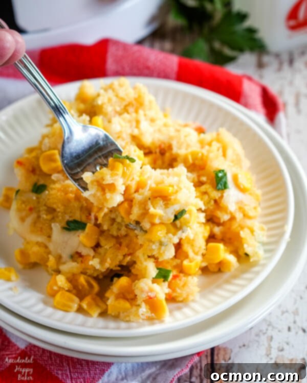 Creamy Slow Cooker Corn Bake 7 A serving of crockpot corn casserole on a white plate sitting next to a slow cooker.