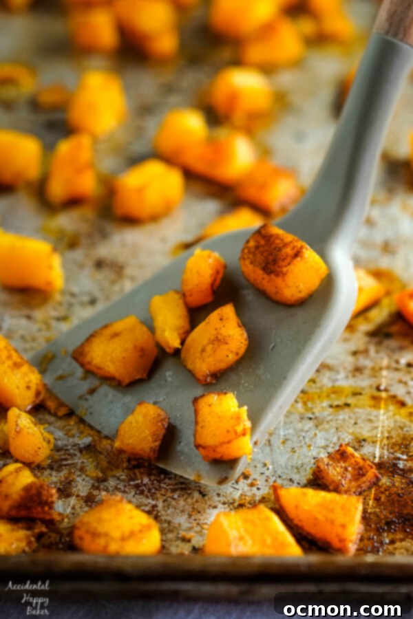 A sheet pan of beautifully caramelized cinnamon and bourbon roasted butternut squash, with a spatula lifting some pieces, highlighting the golden-brown edges and tender texture. 