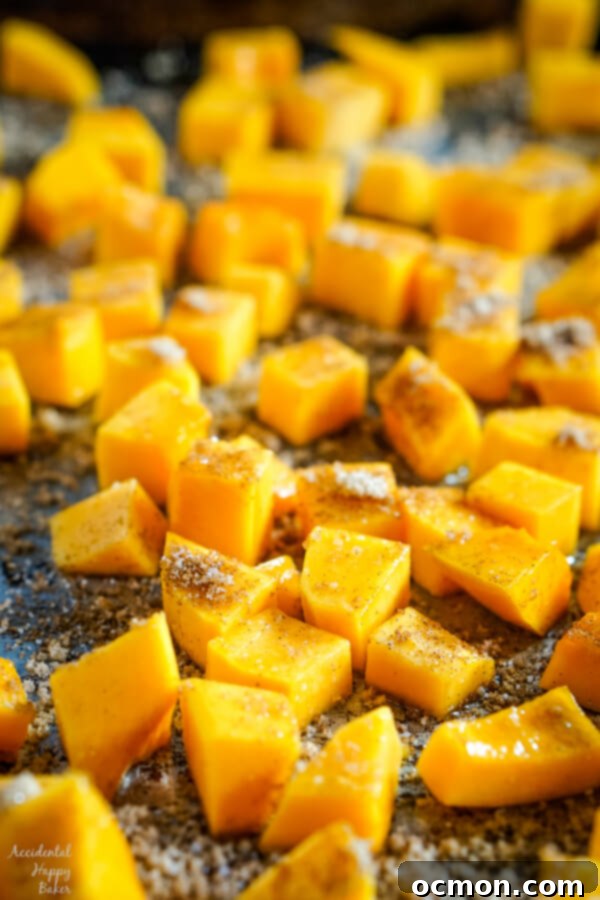 A close-up view of diced butternut squash cubes generously sprinkled with a warm blend of cinnamon, salt, and brown sugar, ready for roasting.