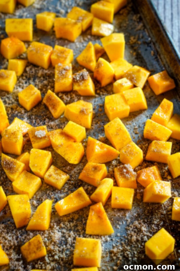 A baking sheet filled with evenly spaced bourbon and cinnamon butternut squash cubes, glistening and ready to be placed into the preheated oven for roasting.