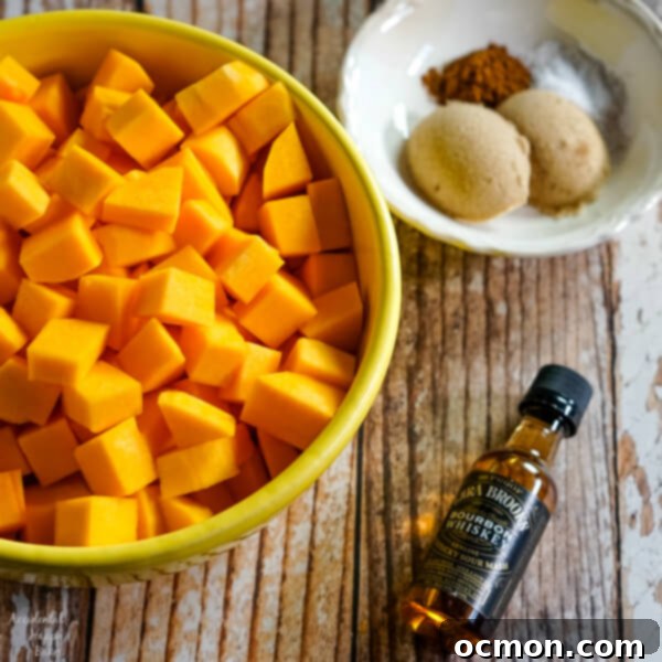 A rustic composition featuring a bowl of peeled and chopped butternut squash, accompanied by a small bottle of bourbon and a separate bowl of cinnamon, brown sugar, and salt, ready for the roasting process.