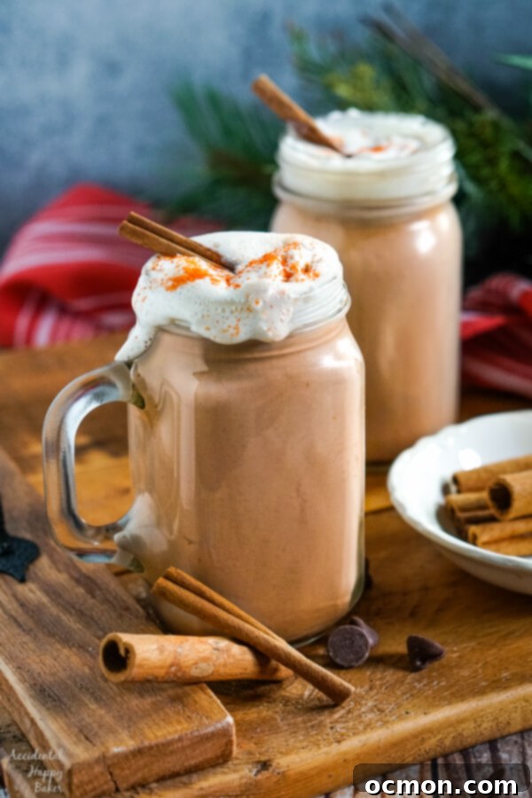 Clear glass mugs of Mexican Hot Cocoa topped with whipped cream and cinnamon sticks on a wooden tray, ready for serving.