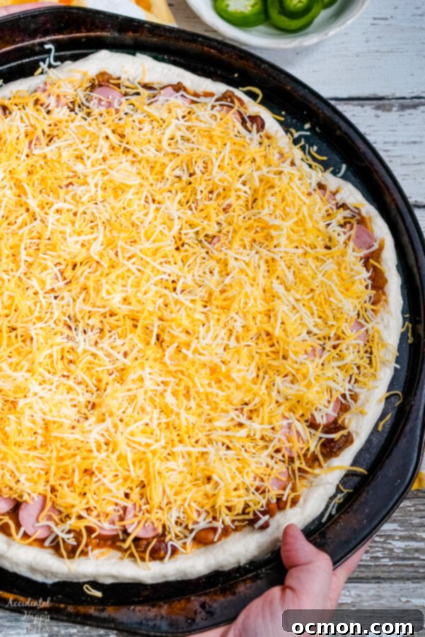 The Chili Dog Pie 6 A generous layer of shredded cheddar cheese completely covers the chili and hot dog toppings on the pizza, ready to be melted and browned in the oven.