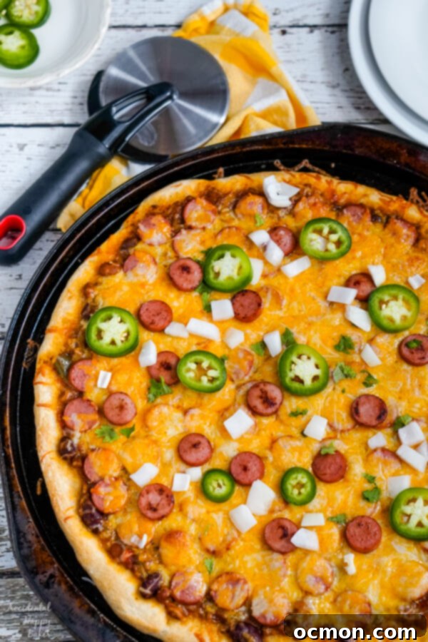 The Chili Dog Pie 9 A beautifully baked chili dog pizza, garnished with fresh chopped jalapenos and diced onions, ready to be sliced and served.