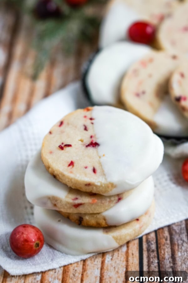 A stack of shortbread cookies on a white napkin next to some fresh cranberries. 