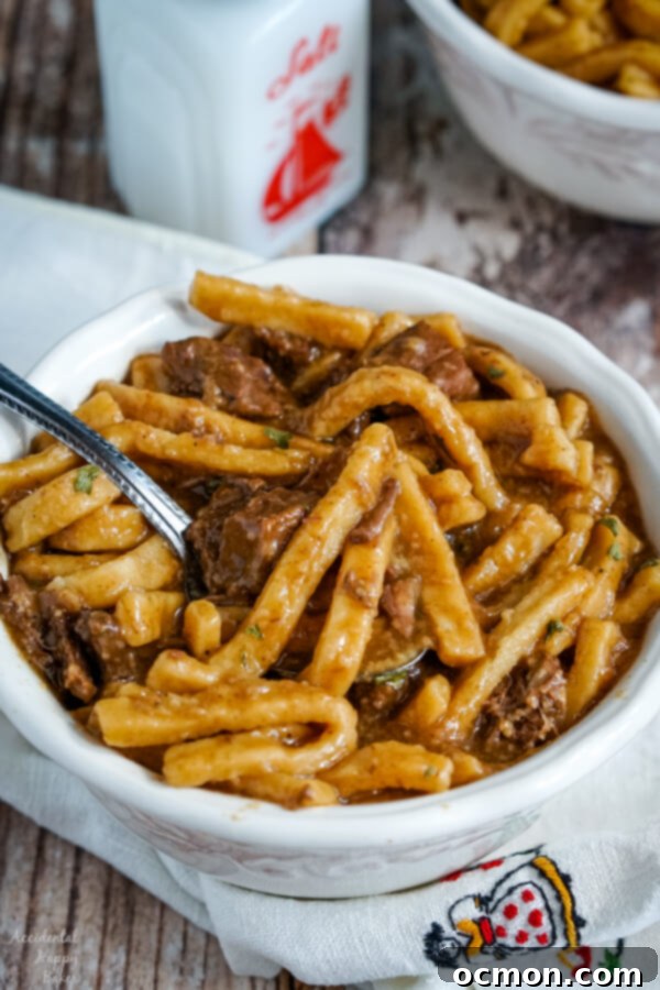 A white bowl full of Beef and Noodles sitting on top of a white cloth napkin.