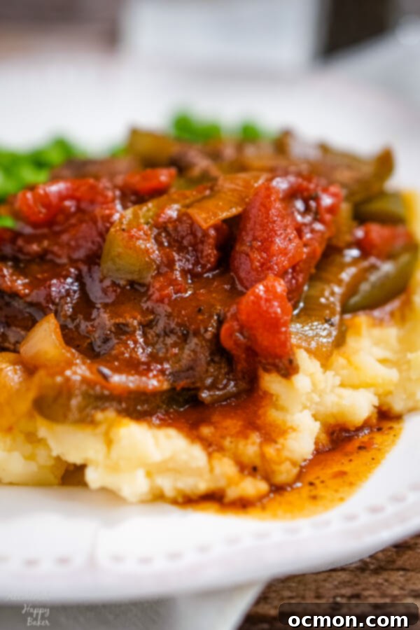 BBQ Swiss Steak with peppers and onions is served up on a pile of cheddar mashed potatoes. 