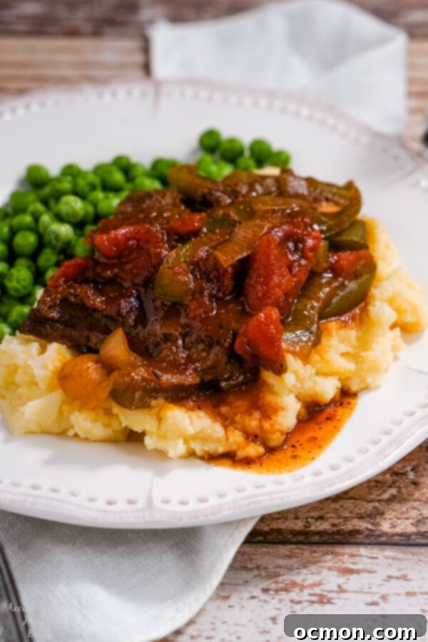 A serving of BBQ Swiss Steak on top of mashed potatoes on a white plate. 