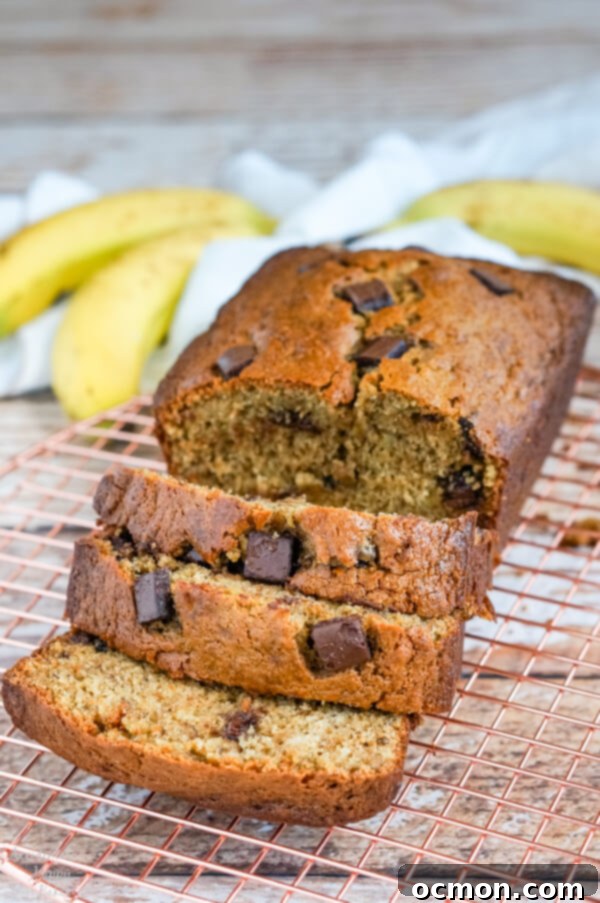 A loaf of chocolate chunk banana bread sliced and sitting on a copper cooling rack.
