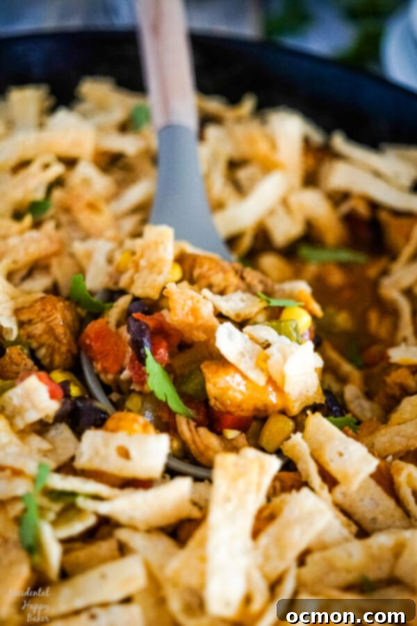 A serving spoon dishing out a serving of Southwestern Egg Roll Casserole from the cast iron skillet, showcasing the golden-brown wonton topping and rich filling.