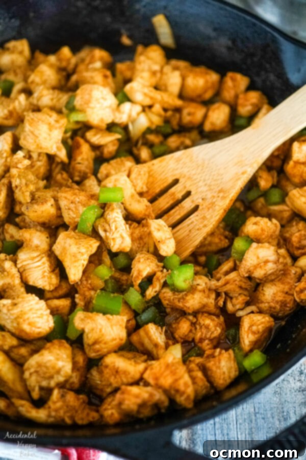 Chicken is browned and then cooked with onions and bell peppers in a cast iron skillet, emitting an aromatic steam.