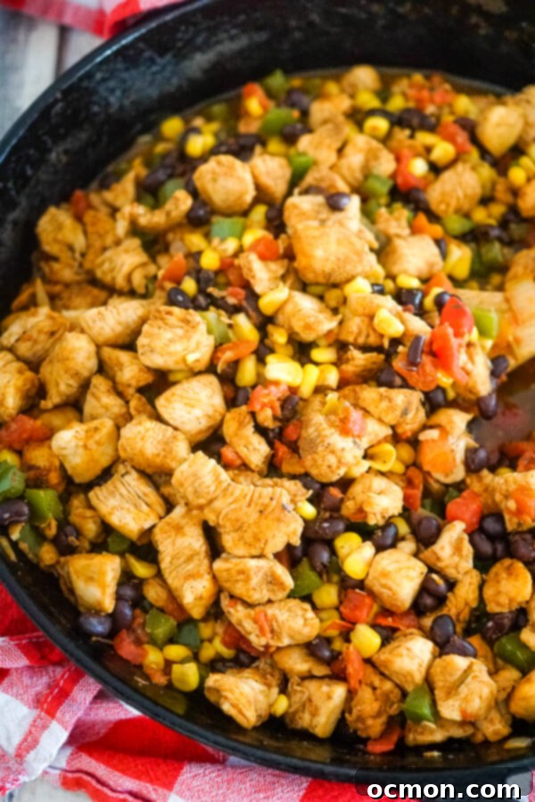 A cast iron skillet full of colorful chicken, black beans, corn, and Rotel, simmering gently on the stovetop.