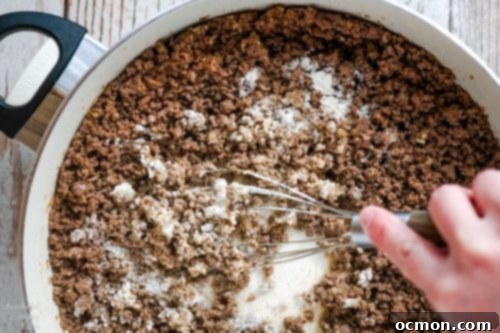 Close-up of ground beef mixture in a skillet with flour being stirred in, preparing the base for a savory sauce.