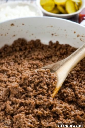 A spoonful of rich, savory ground beef filling being scooped from a skillet, perfect for loose meat sandwiches.