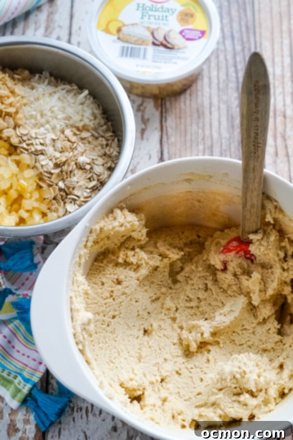 Zesty Lemon Cowboy Cookies 3 A bowl of creamy cookie dough sits beside another bowl brimming with a colorful mix of candied lemon peel, oats, coconut, and crisp rice cereal, ready to be combined.