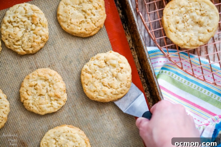 Zesty Lemon Cowboy Cookies 6 A sheet pan filled with golden-brown, freshly baked and cooled cookies, with a spatula gently lifting one cookie to reveal its texture.